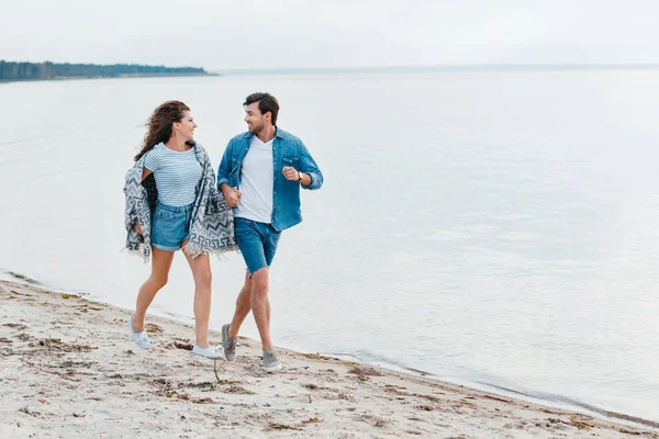 Couple heureux tenant la main et courant sur la plage près de la mer — Photo de stock