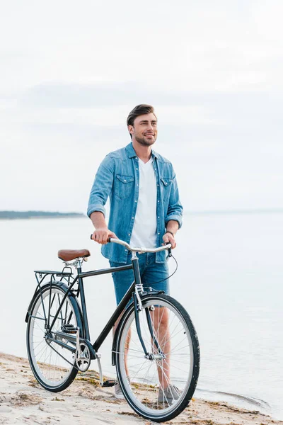 Bonito sorrindo homem andando com bicicleta na praia de areia — Fotografia de Stock
