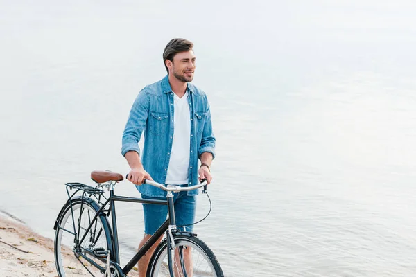 Homem bonito andando com bicicleta na praia de areia — Fotografia de Stock