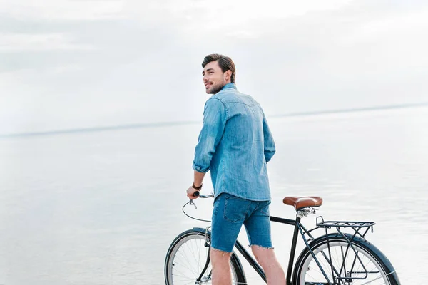 Hombre guapo caminando con bicicleta cerca del mar - foto de stock