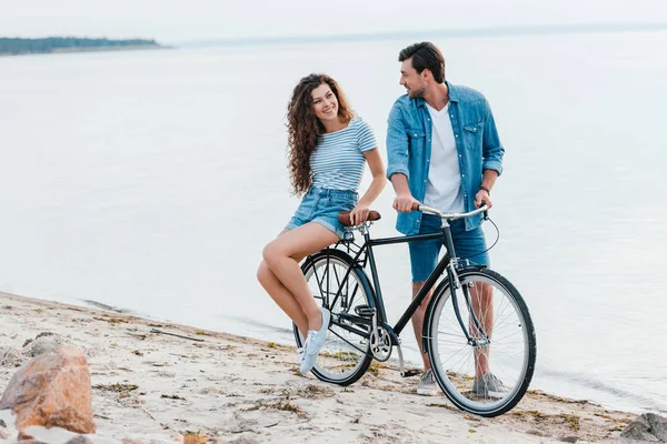 Couple spending time together with bike on beach near sea — Stock Photo