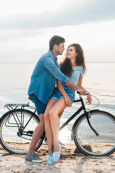 Happy couple sitting on bike near sea and looking at each other — Stock Photo