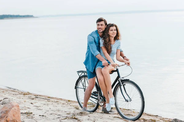 Young couple sitting on bicycle on beach near sea — Stock Photo
