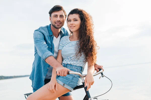 Happy young couple sitting on bike near sea — Stock Photo