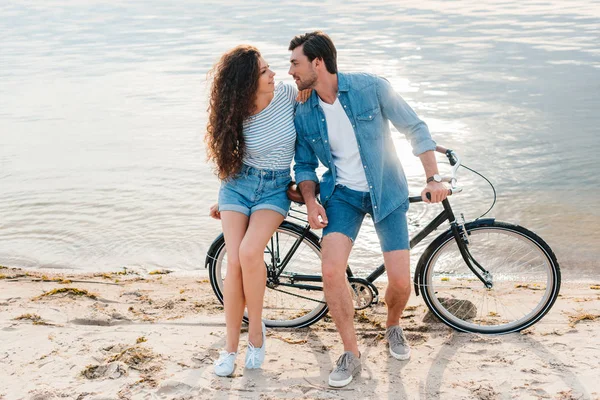 Hermosa pareja sentados juntos en bicicleta en la playa cerca del mar - foto de stock