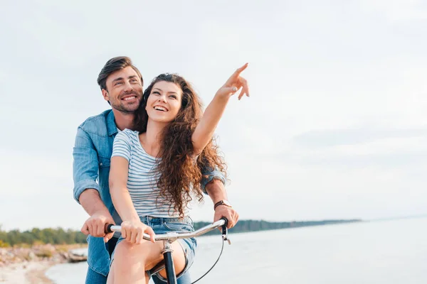 Coppia seduta in bicicletta sulla spiaggia mentre la ragazza punta lontano — Foto stock