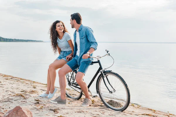 Cheerful couple sitting on bicycle on beach near sea — Stock Photo