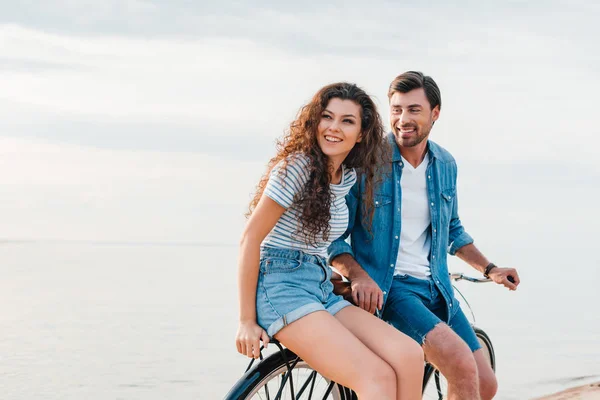 Guapo novio y feliz novia sentado en bicicleta cerca del mar - foto de stock