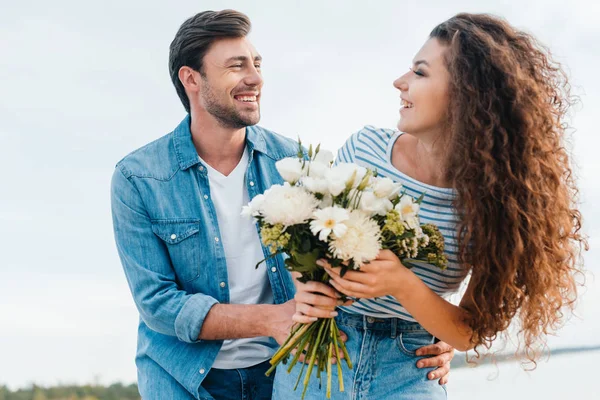 Glückliches Paar umarmt und hält Blumenstrauß zusammen am Meer — Stockfoto