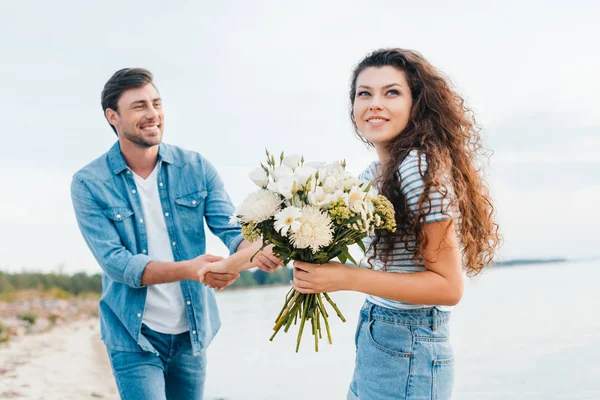 Jeune copine avec bouquet tenant la main avec petit ami — Photo de stock