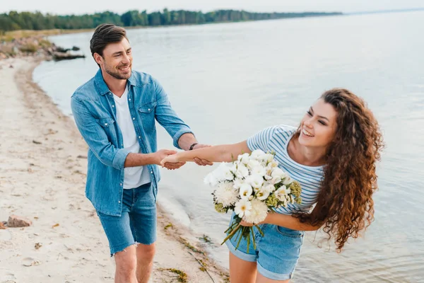 Beautiful happy girlfriend with bouquet holding hands with boyfriend — Stock Photo