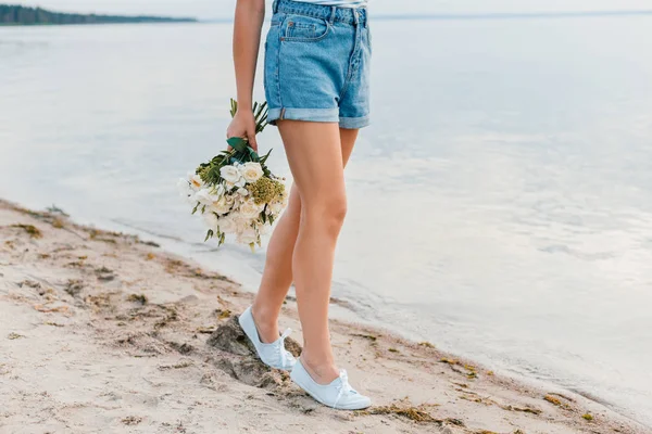 Низький вид на дівчину з букетом, що йде на пляжі біля моря — стокове фото
