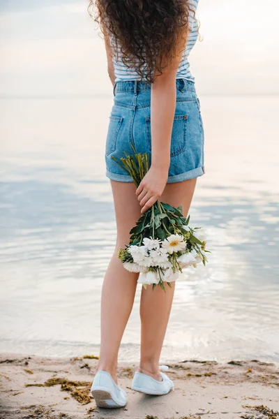 Vue partielle de la femme avec bouquet debout sur le bord de la mer — Photo de stock