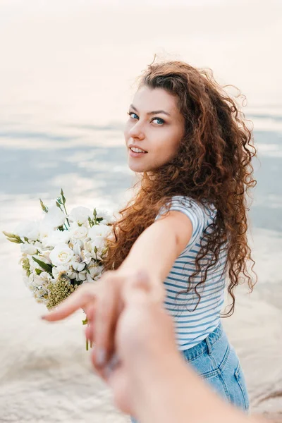 Attractive curly girlfriend with bouquet holding hands with boyfriend — Stock Photo