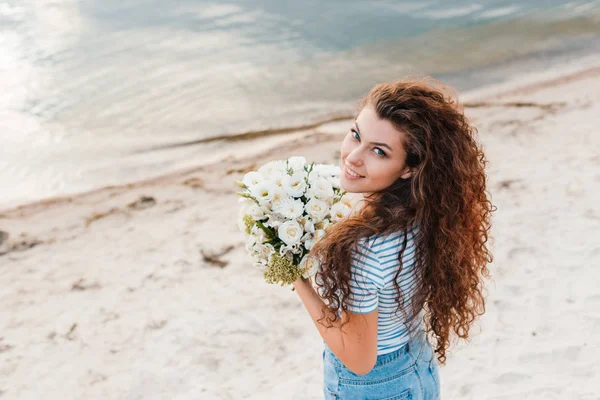 Menina sorridente atraente com buquê de flores posando na praia — Fotografia de Stock