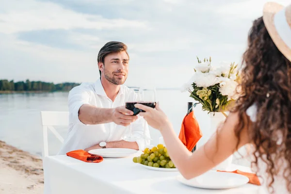 Young couple clinking with wineglasses during romantic date on beach — Stock Photo