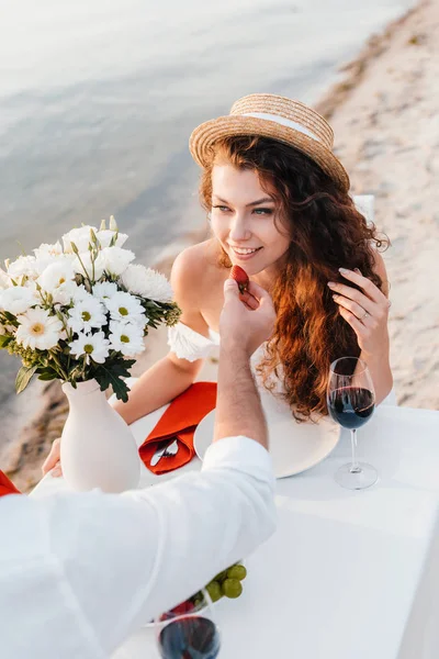 Man feeding happy girlfriend with fresh strawberry during romantic date on beach — Stock Photo