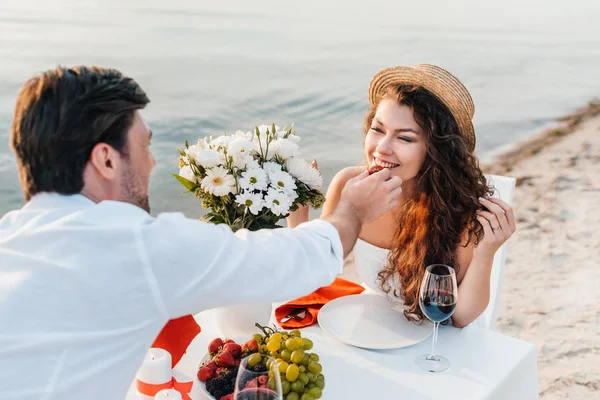 Mann füttert lächelndes Mädchen bei romantischem Date am Strand mit Erdbeere — Stockfoto