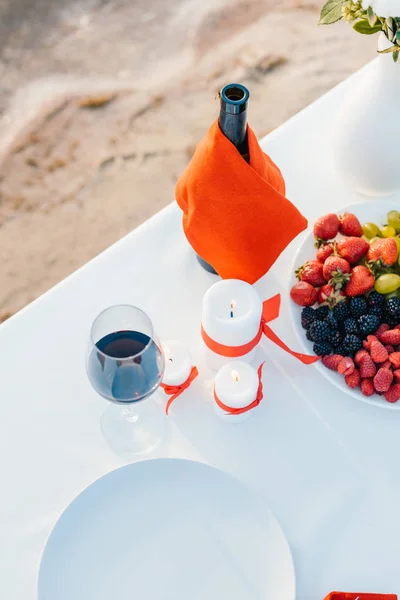 Champagne, fruits and candles on table for romantic date on beach — Stock Photo