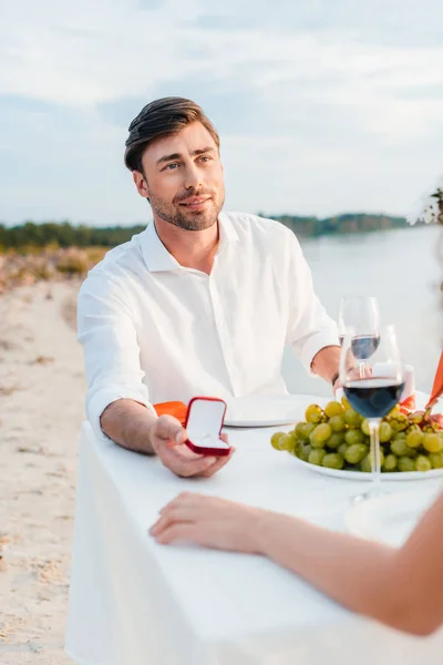 Schöner Mann macht Frau bei romantischem Date am Strand einen Heiratsantrag mit Ring — Stockfoto