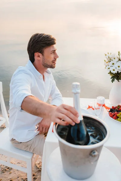 Bel homme prenant bouteille de champagne à table sur le bord de la mer — Photo de stock