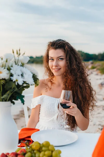 Attraktives lächelndes Mädchen mit Weinglas bei romantischem Date am Strand — Stockfoto
