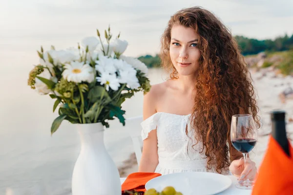 Attractive happy girl with glass on wine on romantic date on beach — Stock Photo