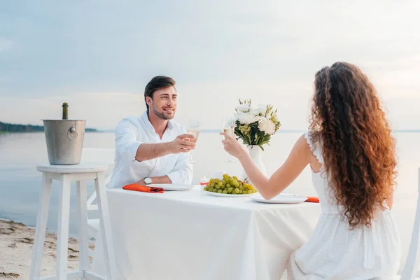 Novio y novia tintineo con copas de champán durante la cita romántica en la orilla del mar - foto de stock