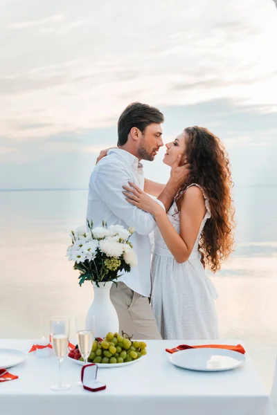 Happy couple hugging and kissing near table with proposal ring — Stock Photo