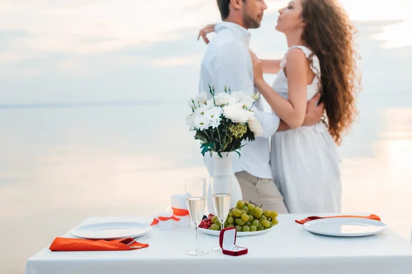 Selective focus on couple hugging near table with proposal ring — Stock Photo