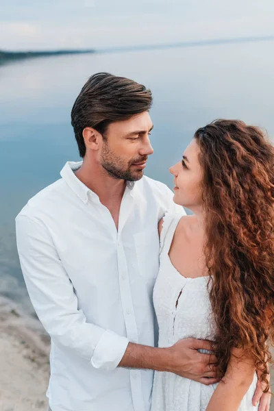 Junges romantisches Paar schaut einander an und umarmt sich am Strand — Stockfoto