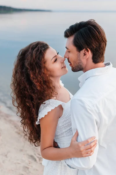 Feliz pareja romántica mirándose y abrazándose en la orilla del mar - foto de stock