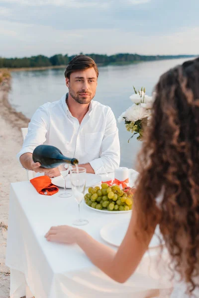 Man pouring champagne for girlfriend during romantic date on beach — Stock Photo