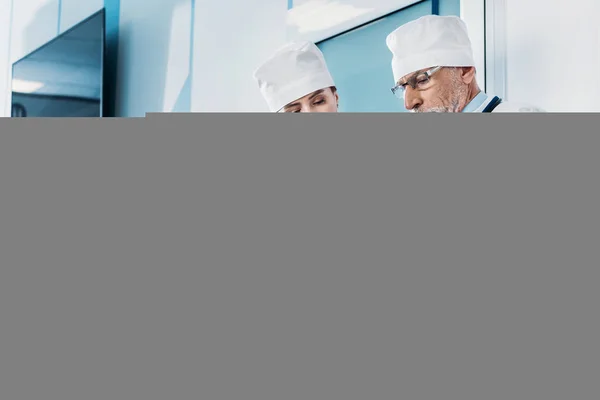 Middle aged male doctor showing clipboard to female colleague in hospital corridor — Stock Photo