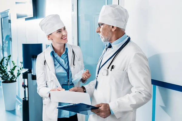 Médicos do sexo masculino e feminino com área de transferência tendo discussão no corredor hospitalar — Fotografia de Stock