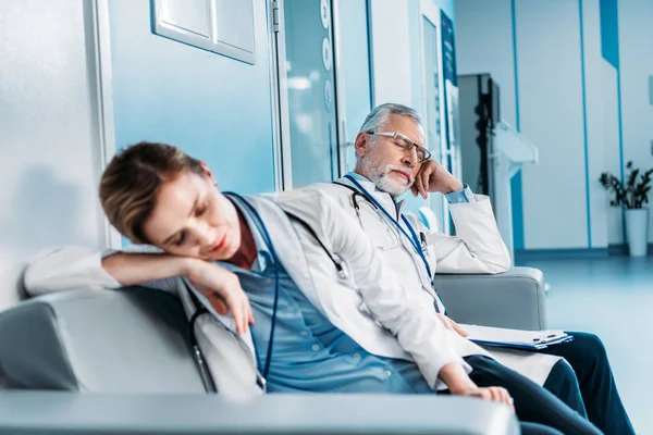 Exhausted male and female doctors sleeping on sofa in hospital corridor — Stock Photo