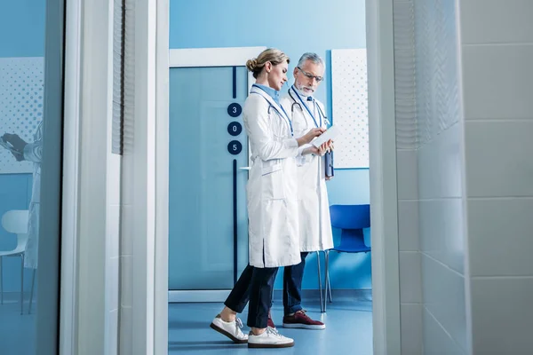 Doctora mostrando tableta digital a colega masculino en corredor hospitalario - foto de stock