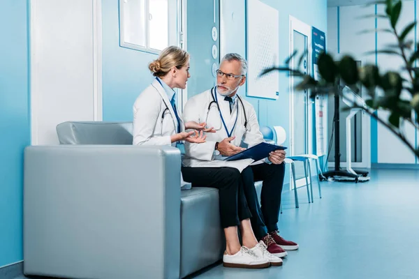 Emotional female doctor having discussion with male colleague on sofa in hospital corridor — Stock Photo
