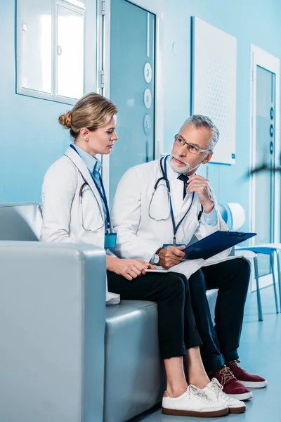 Male and female doctors talking on couch in hospital corridor — Stock Photo