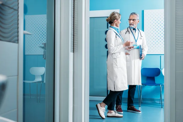 Улыбающиеся врачи-женщины и мужчины разговаривают в больничном коридоре — стоковое фото