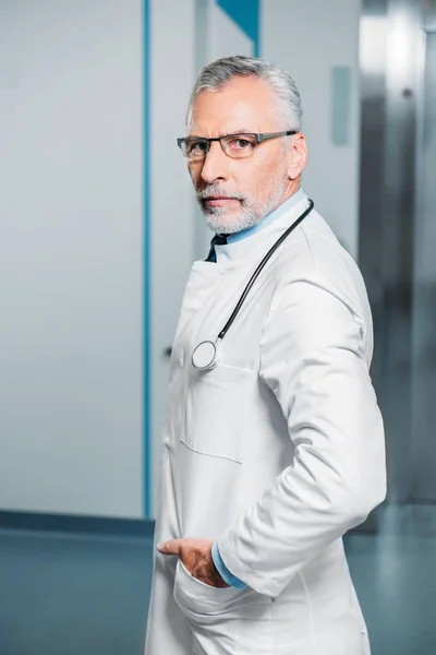 Впевнений чоловік середнього віку лікар зі стетоскопом над шиєю дивиться на камеру в лікарні — стокове фото