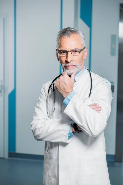 Thoughtful middle aged male doctor with stethoscope over neck looking at camera in hospital — Stock Photo