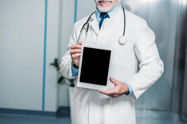 Partial view of mature male doctor with stethoscope over neck showing digital tablet with blank screen in hospital — Stock Photo