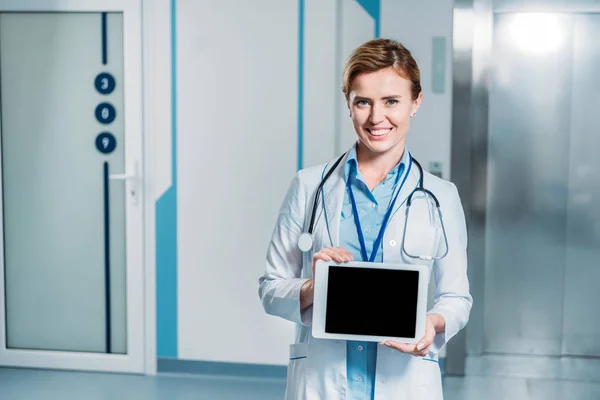 Médecin femme souriante avec stéthoscope au-dessus du cou montrant tablette numérique avec écran blanc à l'hôpital — Photo de stock