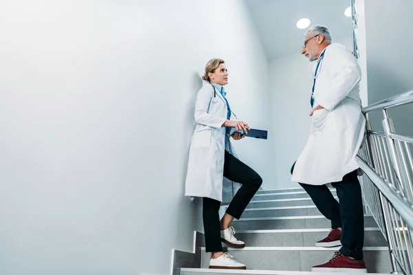 Side view of male and female doctors talking on staircase in hospital — Stock Photo