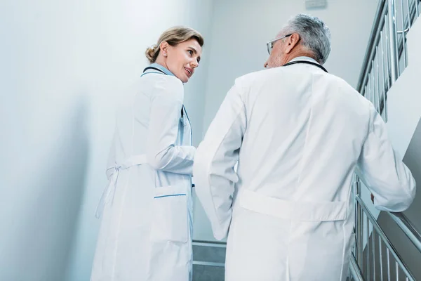Vista trasera de los médicos masculinos y femeninos hablando y caminando por las escaleras en el hospital - foto de stock