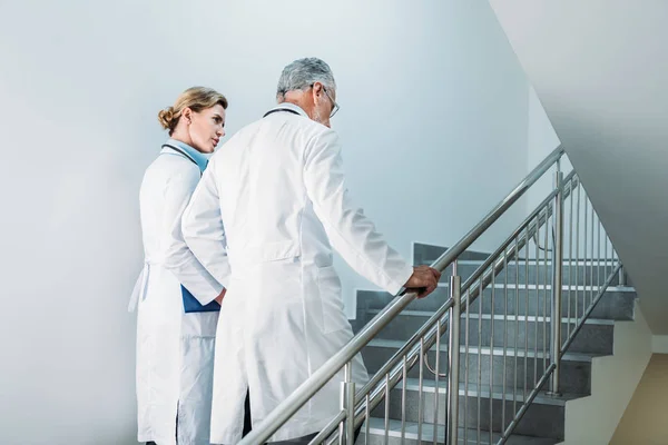 Vista trasera de los médicos masculinos y femeninos caminando por la escalera en el hospital - foto de stock