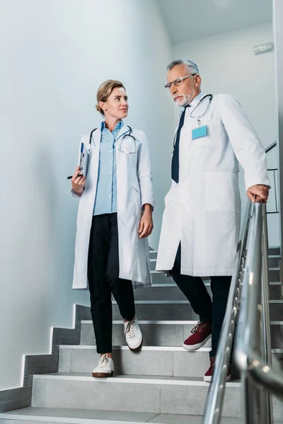 Médicos hombres y mujeres con portapapeles caminando por las escaleras en el hospital - foto de stock