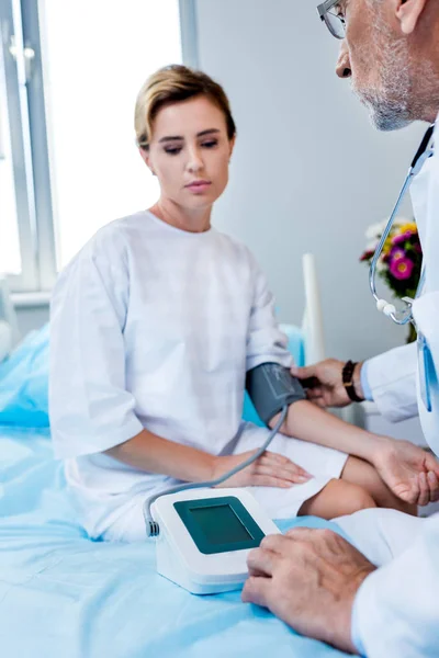 Частковий вигляд лікаря-чоловіка, що вимірює тиск пацієнта жінки за тонометром у лікарняній кімнаті — стокове фото