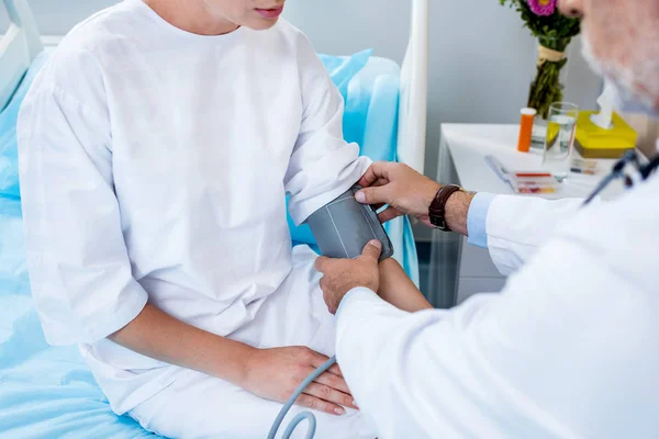 Visão parcial do médico de meia idade do sexo masculino colocando no dispositivo para medir a pressão sobre a mão paciente do sexo feminino no quarto do hospital — Fotografia de Stock